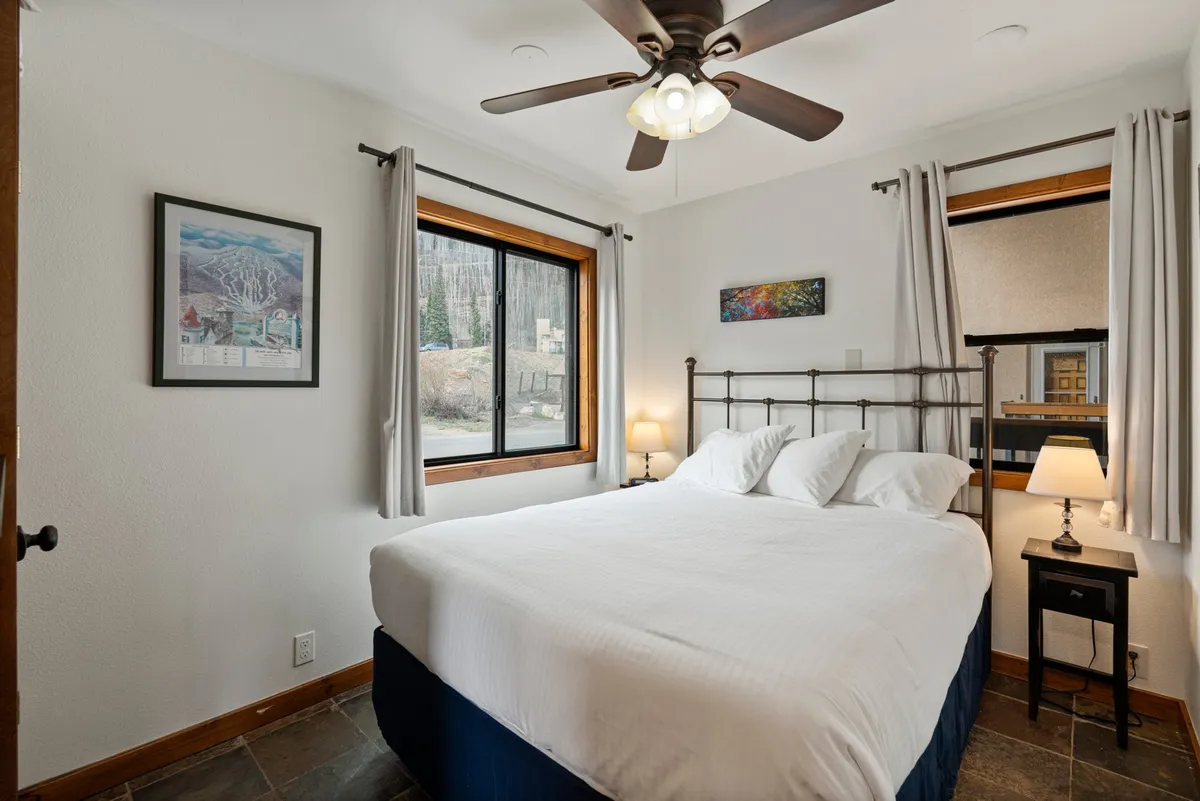 A serene bedroom with a queen bed, illuminated by natural light from a window and adorned with tasteful artwork and a bedside lamp. The space exudes comfort and tranquility, ideal for restful sleep and rejuvenation.