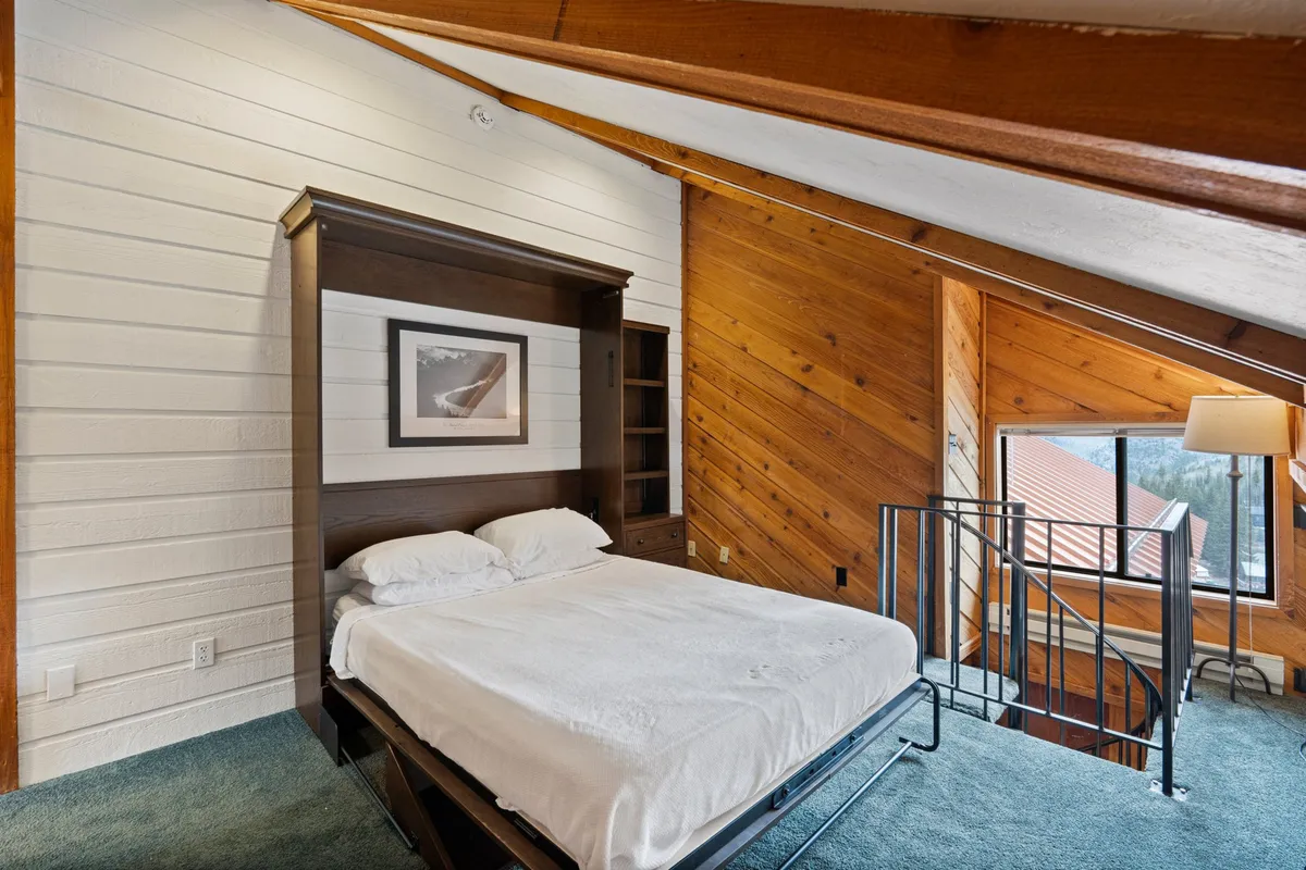 A flexible sleeping area with a fold-down bed, warm wooden accents, and a sunlit window. The design is both practical and cozy, making it ideal for families or groups needing extra sleeping space.