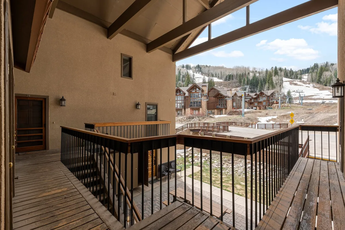 An exterior perspective of a wooden balcony overlooking sweeping mountain vistas. The balcony features room for gathering, with inviting entry doors and space for outdoor relaxation. The surrounding scenery captures the tranquil, awe-inspiring beauty of the Needles Mountains.