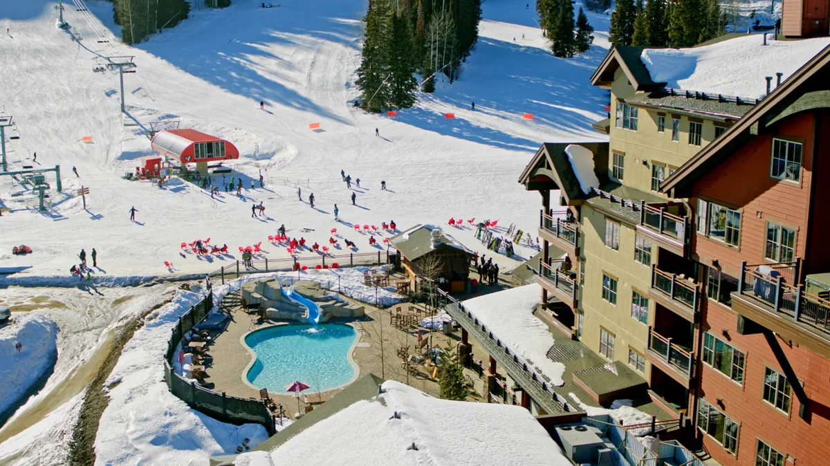 An energetic exterior scene showing ski slopes bustling with activity, a sparkling swimming pool, a ski lift, and a welcoming lodge. The landscape is alive with both winter and summer recreation, illustrating the fun and communal spirit of the area.