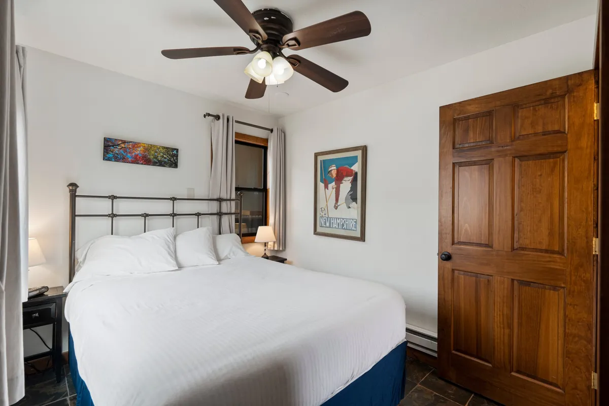 A cozy bedroom showcasing a comfortable queen bed, nightstands, a ceiling fan, and a window letting in soft daylight. The room's decor is soothing, making it perfect for relaxation and unwinding after a day of adventure.